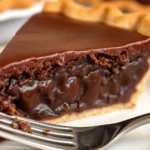 Close-up of a perfectly sliced old fashioned chocolate pie showing creamy dark chocolate filling, flaky golden crust, and glossy surface, served on white plate with fork