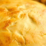 Close-up of golden-brown homemade pie crust with crimped edges, showing flaky layers and butter texture on ceramic pie dish